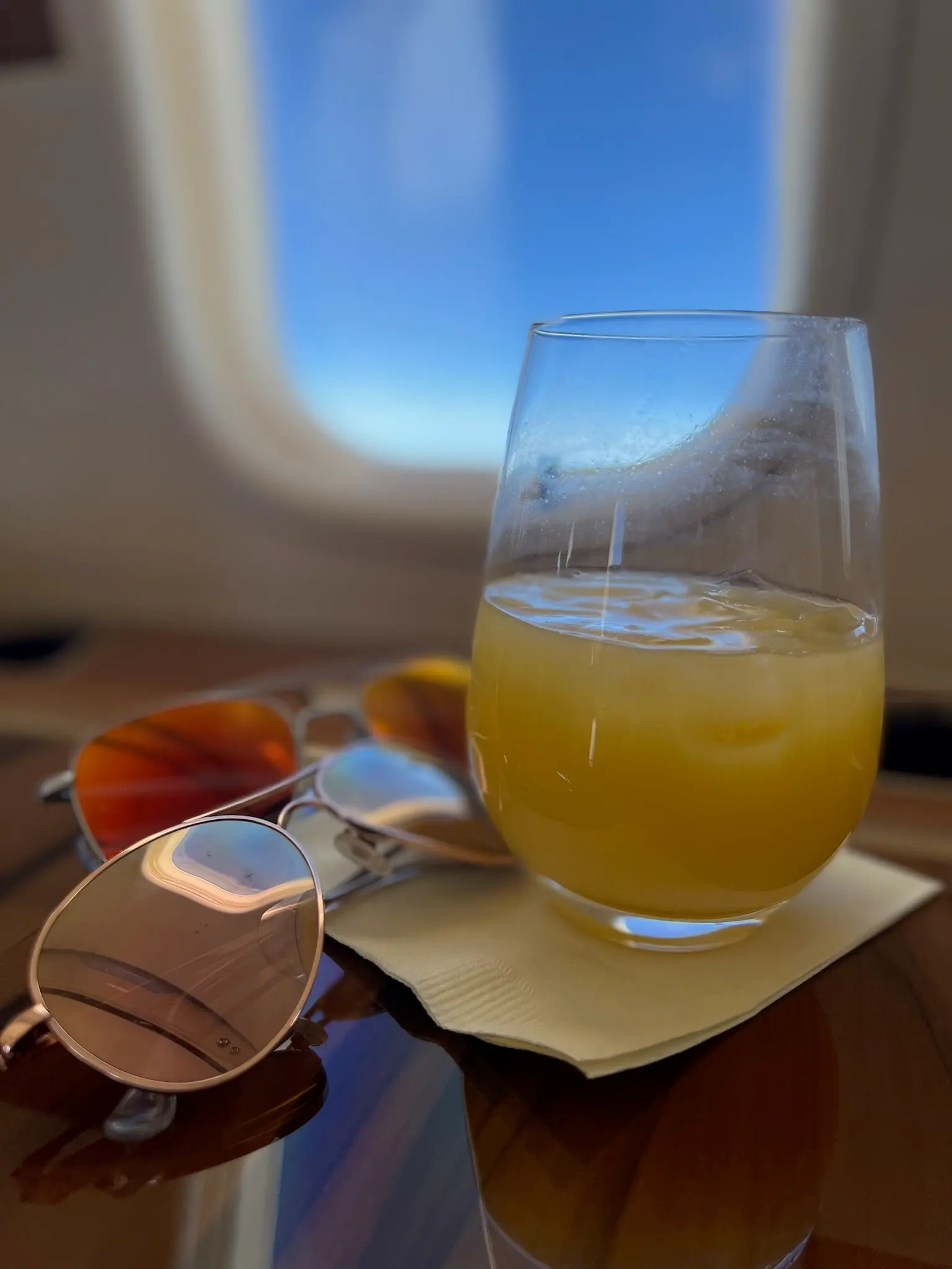 A drink and sunglasses beside a private jet window